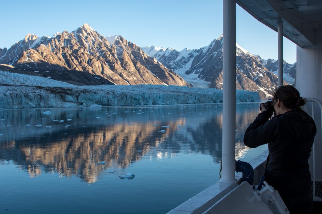 Passenger on ship taking photo of glacier & mountains. 