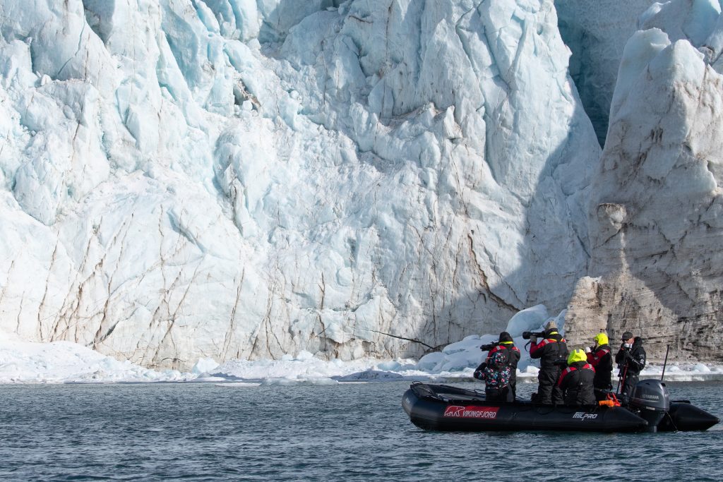 A zodiac on the water in front of huge glacier face.