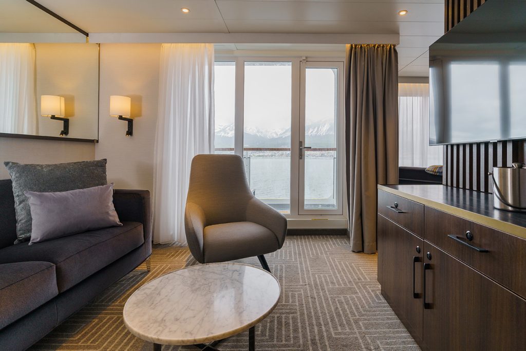 Sitting area in Owner's Suite on Ultramarine with couch, chair and floor to ceiling window leading to  balcony. 