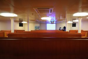 Lecture Room on Ortelius with red bench seating and large TV. 