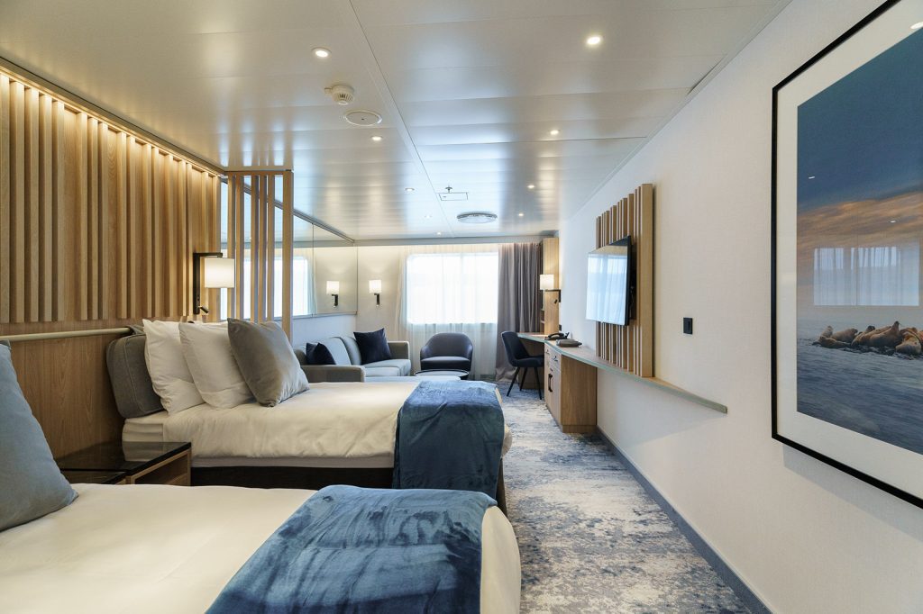 Explorer Suite on the ship Ultramarine showing 2 single beds, couch, desk and window. 