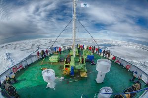 Overhead view of the bow on the ship Ortelius with passengers looking out at pack ice. 