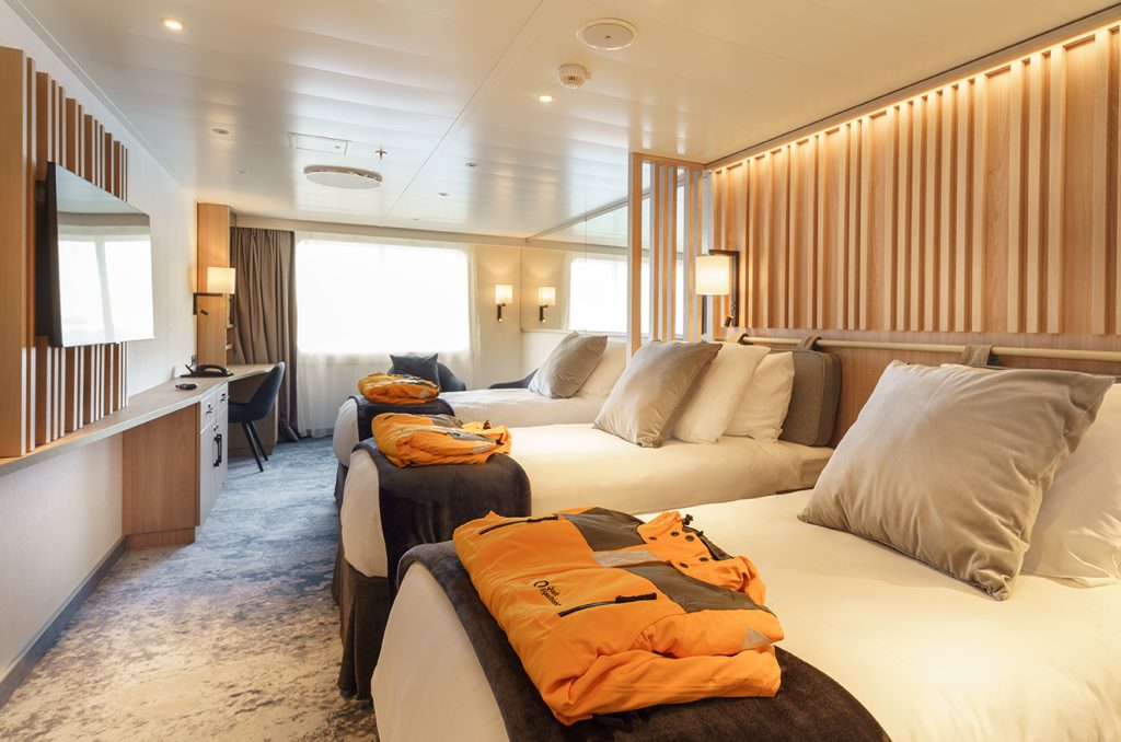Explorer Triple cabin showing 3 single beds and yellow parkas folder on beds. 