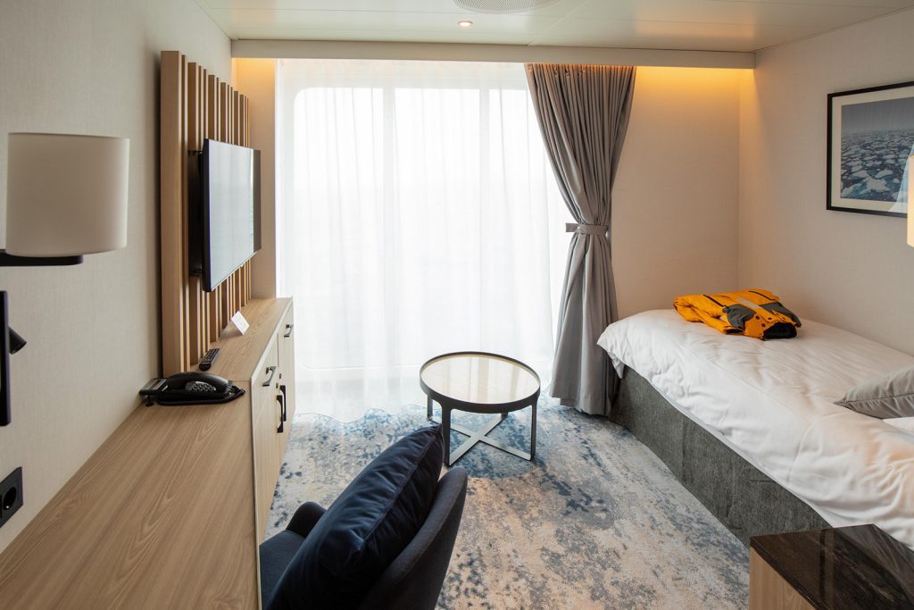 Solo Panorama cabin on Ultramarine showing 1 single bed, tv, small table and large window. 