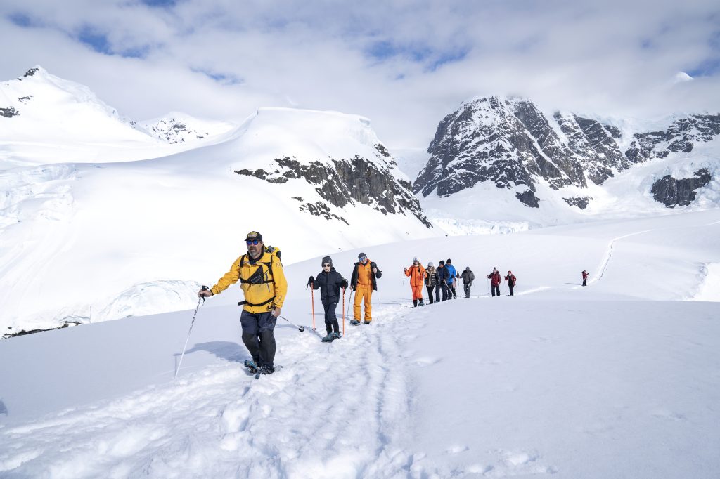 A line of people snowshoeing in Antarctica with mountains in background