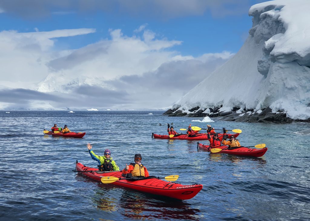 Kayakers on the water next to an ice wall. 