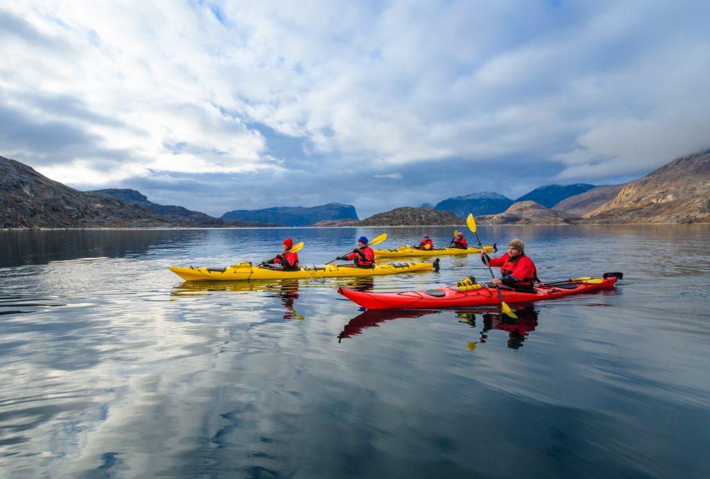 Kayakers paddling in calm water with mountains in background.