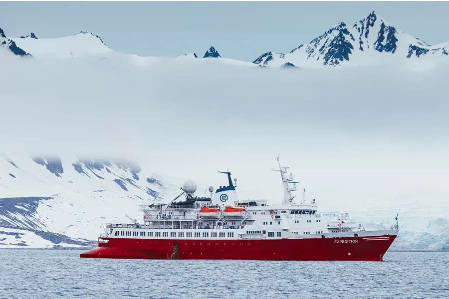 Photo of the ship Expedition on the water with snow capped mountains in the background.