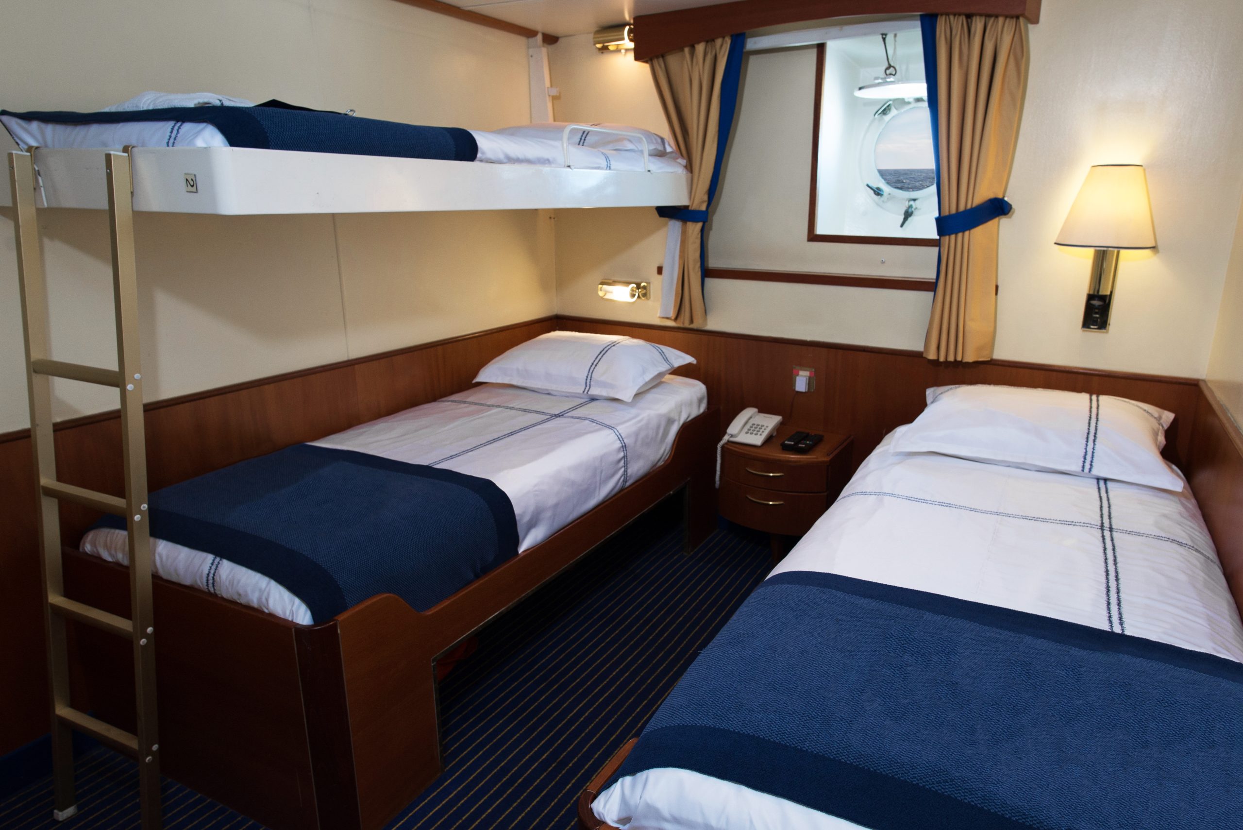 Triple cabin showing 2 lower berths, 1 upper berth and a porthole window.