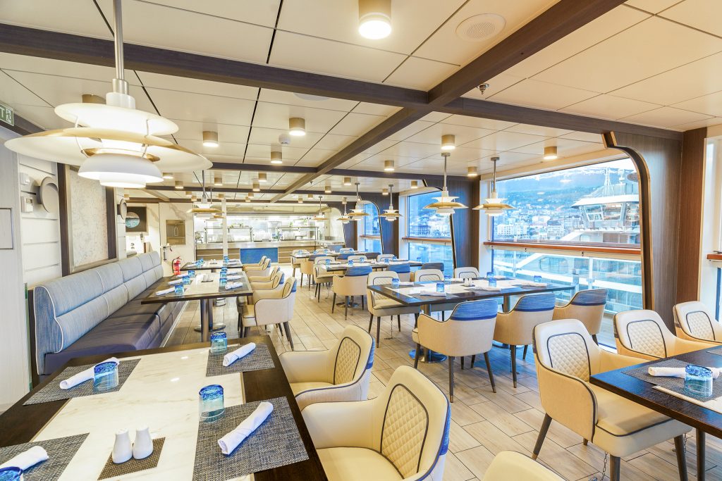 Tables and chairs with floor to ceiling windows in Observation Bistro on Ocean Explorer. 