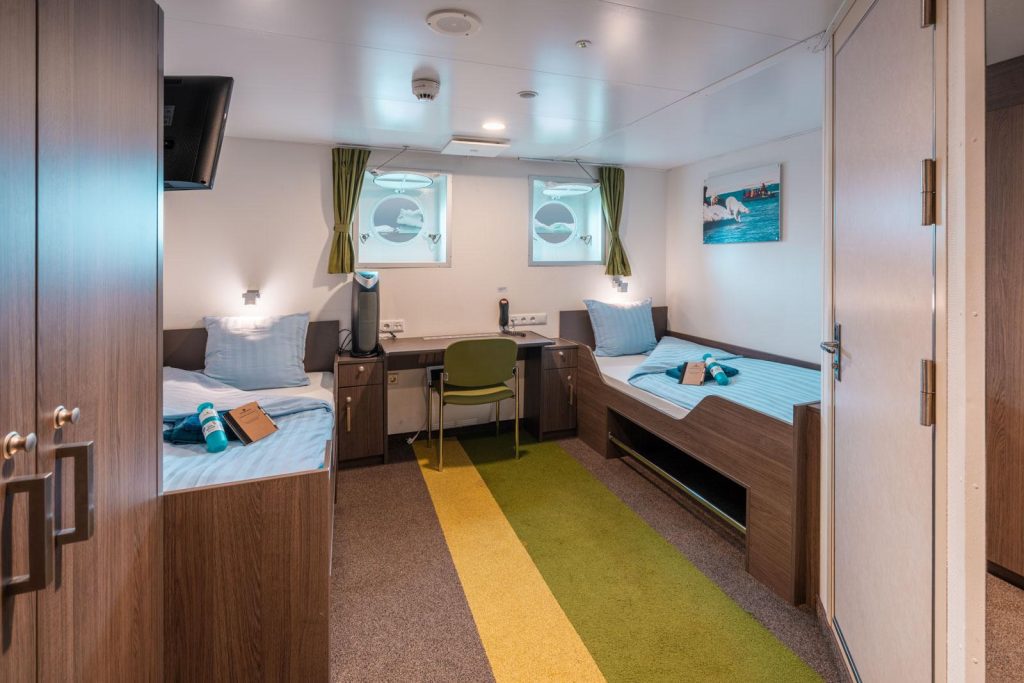 interior of a twin porthole cabin on Ortelius showing 2 twin beds, small desk and 2 portholes