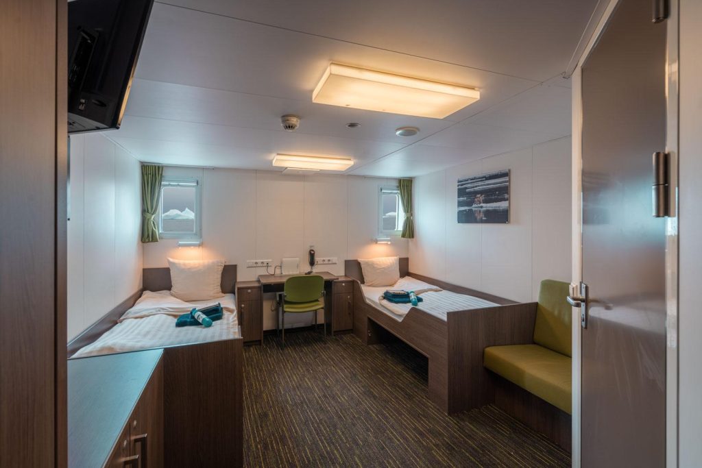 Interior cabin space with 2 single beds, 2 windows and bathroom door.