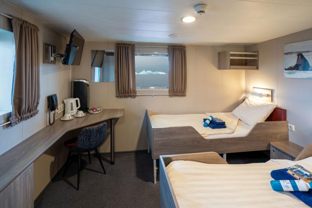 Interior of a Twin Deluxe cabin on the Plancius showing 2 twin beds, 2 windows and desk.
