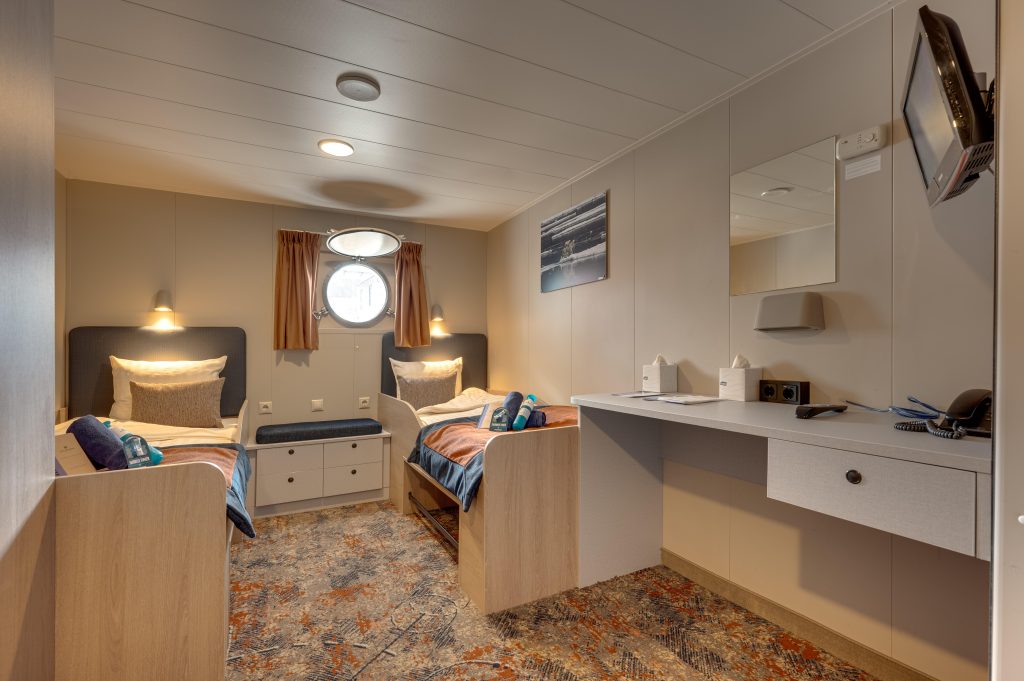 Twin Porthole cabin on the Plancius with 2 twin beds, desk, tv and porthole window.