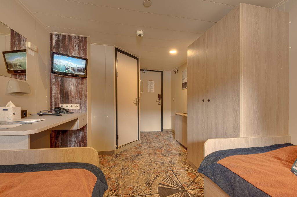 interior of twin porthole cabin on Plancius showing the end of 2 twin beds, small TV on wall, closet and 2 closed doors.
