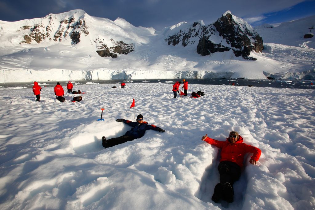 Guest laying down in snow with mountains in bakcground
