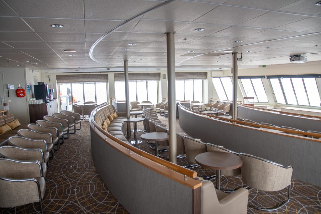 Panorama Lounge onboard the Seaventure showing tiered rows of seats, large windows and coffee bar. 
