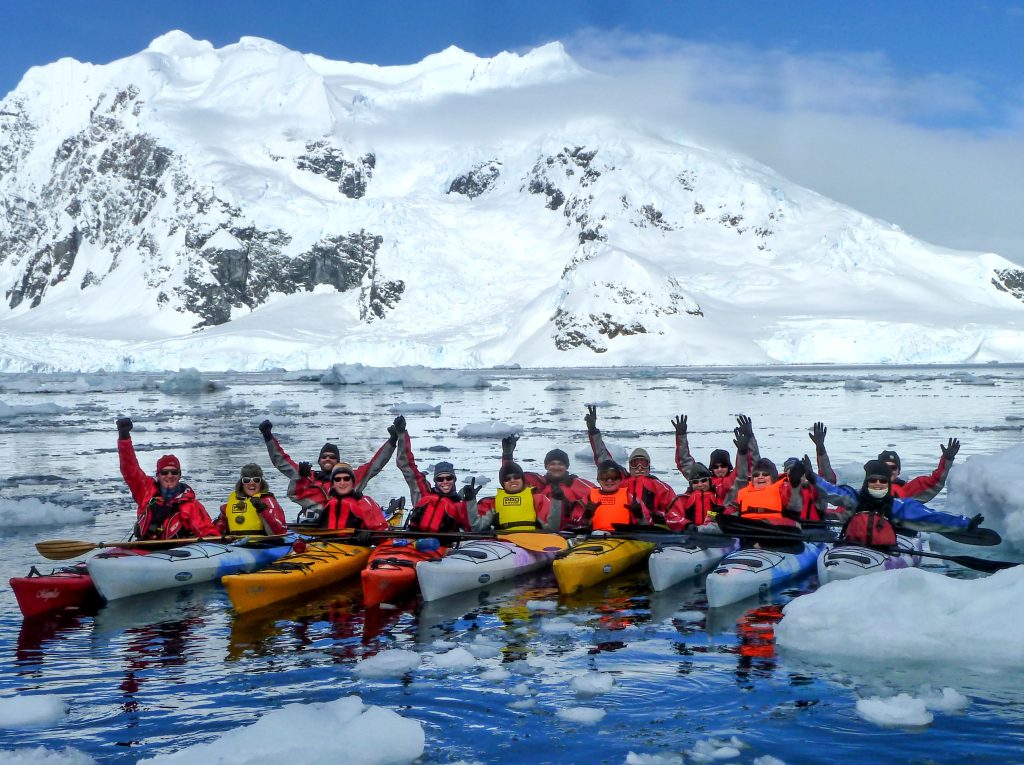 kayakers lined up on the water in Antarctica with snow covered mountain in background