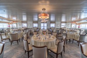 Greg Mortimer dining room with various circular tables, white table cloths, chairs and large windows. 