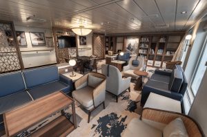 Greg Mortimer library with blue couches, tan chairs, coffee tables and a floor to ceiling bookshelf. 