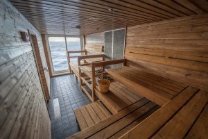 Wooden benches and floor to ceiling window with sea view from the interior of the sauna on Greg Mortimer. 