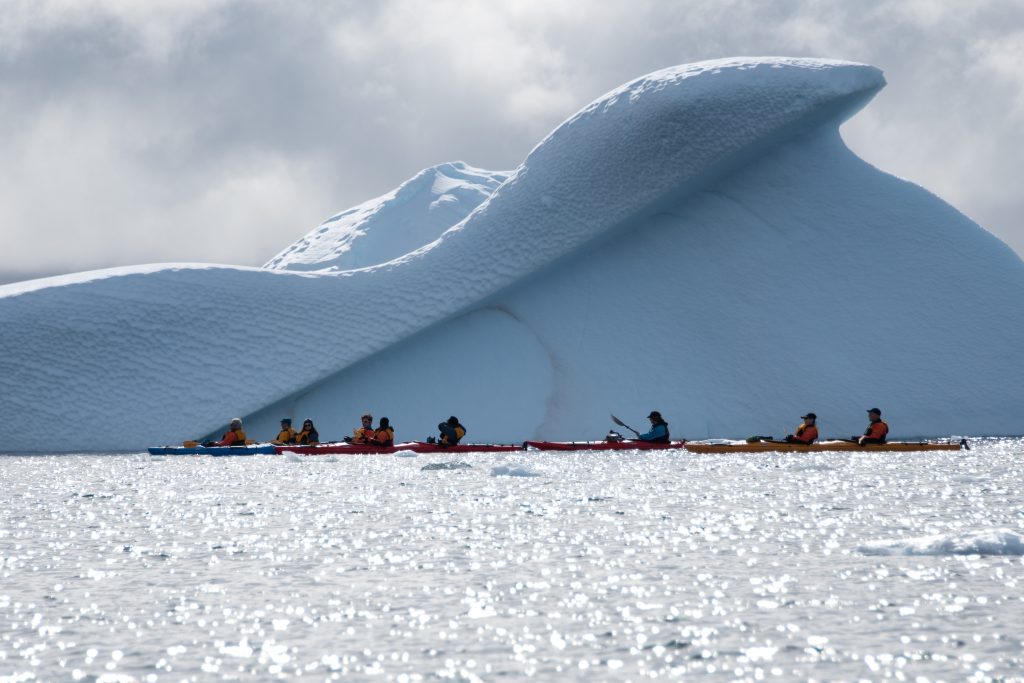 Kayakers on the water in front of large iceberg. 
