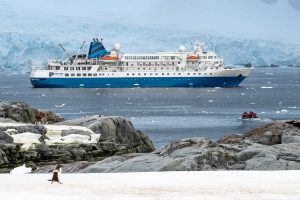 The ship Seaventure anchored in Antarctica with penguins on shore. 