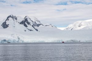 Rugged snow covered alpine peaks with glaciers flowing to water.