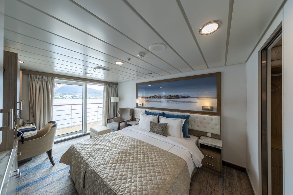 interior of bedroom of Captain's Suite on Greg Mortimer showing 1 king bed and sliding glass door leading to balcony. 