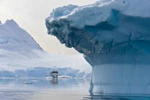 The ship Greg Mortimer on the water framed by large iceberg.