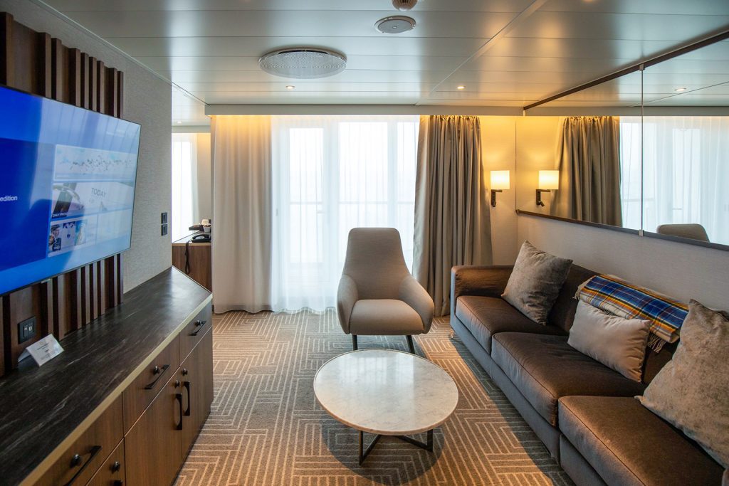 Sitting area with sofa, coffee table and TV in the Ultra Suite onboard the ship Ultramarine. 