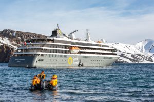 A zodiac on the water cruising towards the ship World Explorer. 