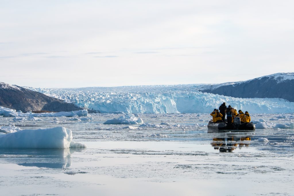 A zodiac in the icy waters in front of large glacier in West Greenland.