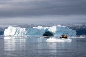 A zodiac cruising near a massive iceberg in West Greenland. 