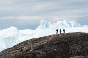 Three guests standing on shore gazing at massive icebergs at Illulissat. 