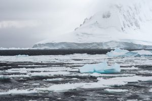 A landscape with sea ice, icebergs, large glacier and mountain seen while crossing the Antarctic Circle.