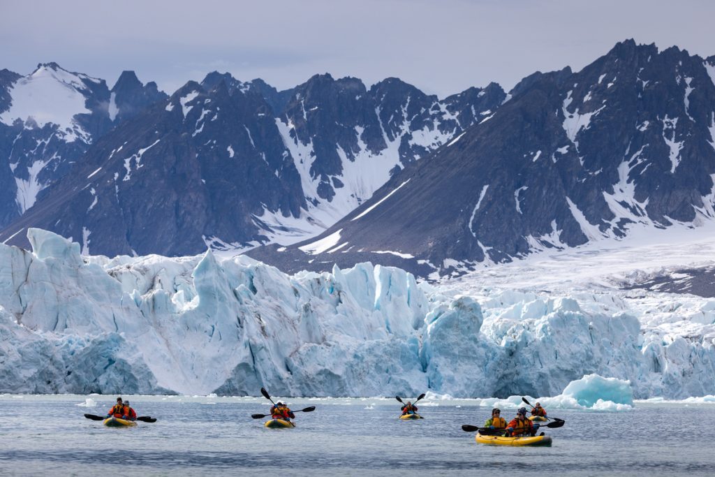Kayakers paddling near large glacier. 