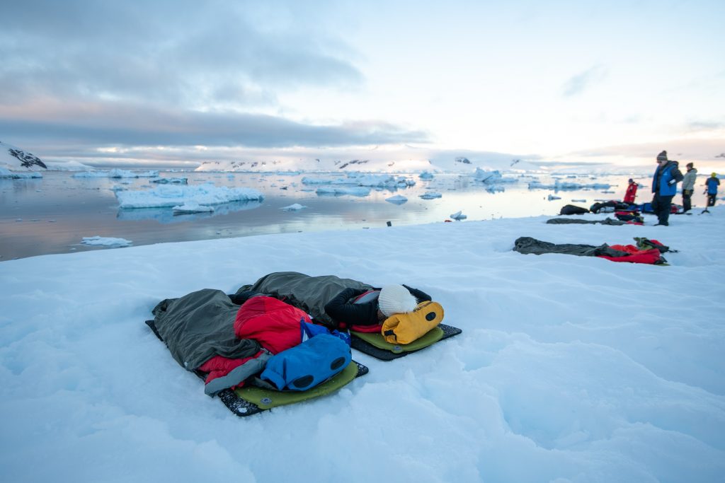 guests camping on the snow in Antarctica with ocean and icebergs in background. 