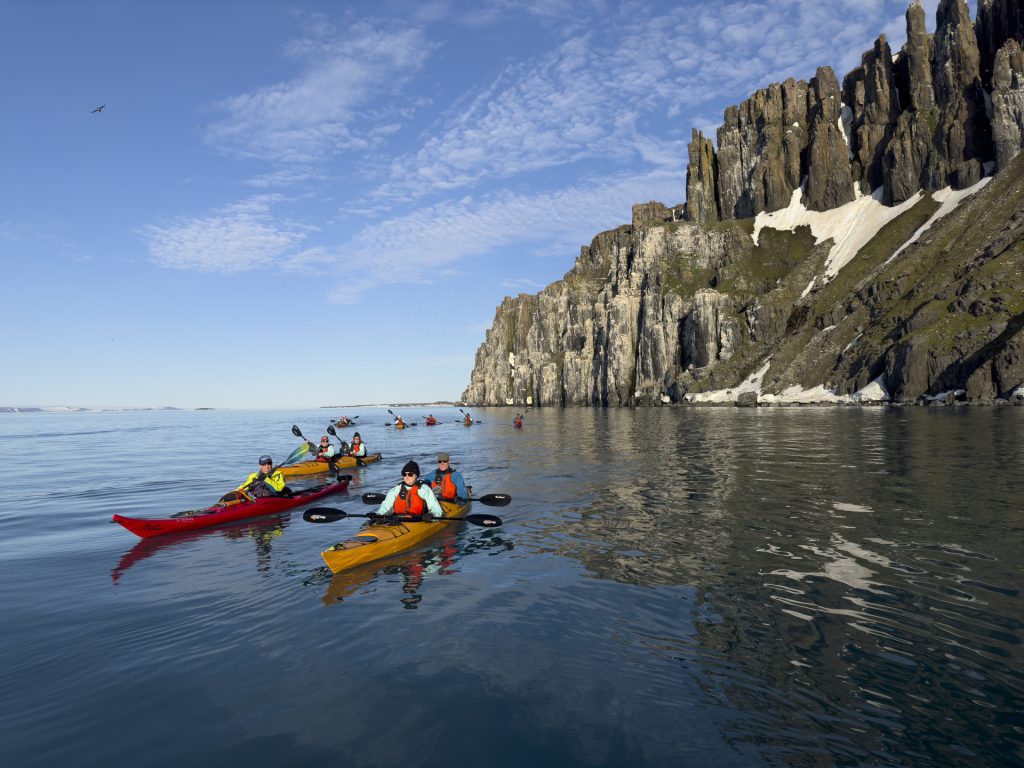Kayakers on the water next to steep cliff.