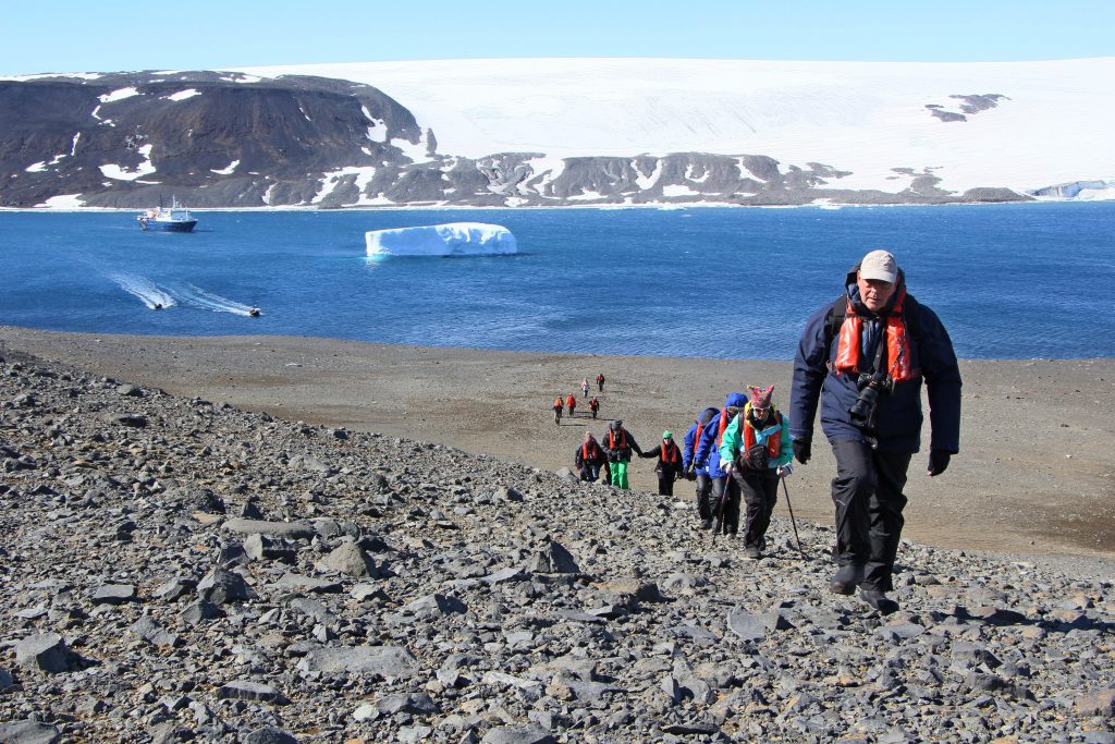 Hikers walking up rocky hillside next to shore.