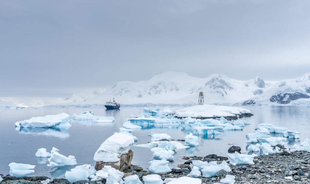 Ship on the water surrounded by icebergs and mountains.