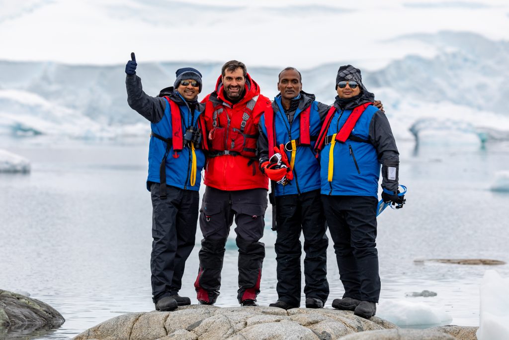 Four guests standing on a large rock in Antarctica. 
