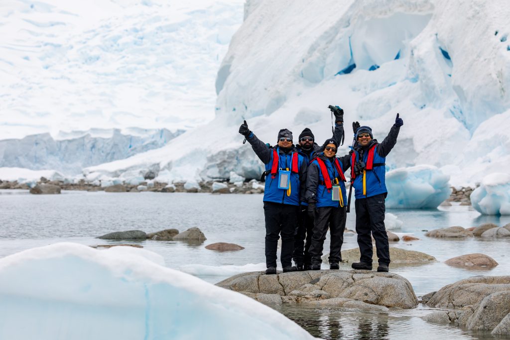 Four passengers standing on a rock with glacier in background.