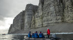 Zodiac near massive rock cliff in the Northwest Passage.