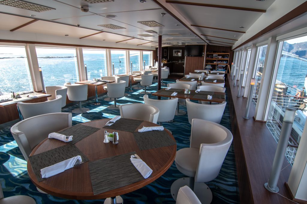 National Geographic Explorer Observation Lounge showing circular wood tables, white chairs and large windows on both sides