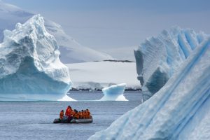 A zodiac full of passengers on the water surrounded by icebergs. 
