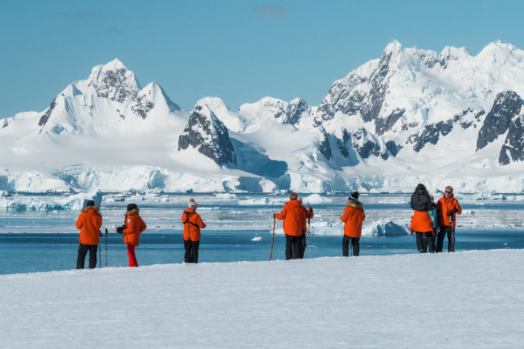 Guests standing in the snow looking at scenic Antarctic landscape.