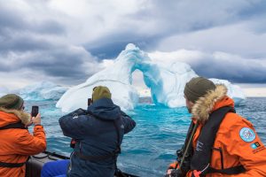 Three guests taking photos of iceberg in Antarctica.
