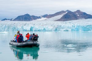 A zodiac on the water with guests gazing at large glacier.