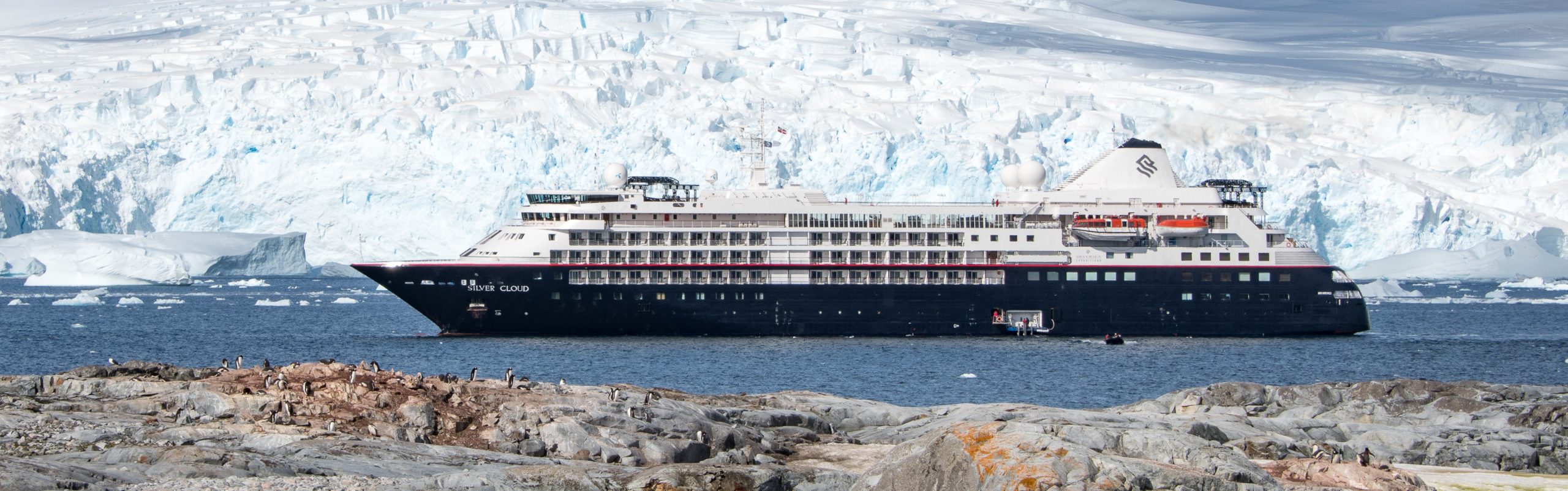 The Silver Cloud in Antarctica with penguins in foreground and glacier in background.